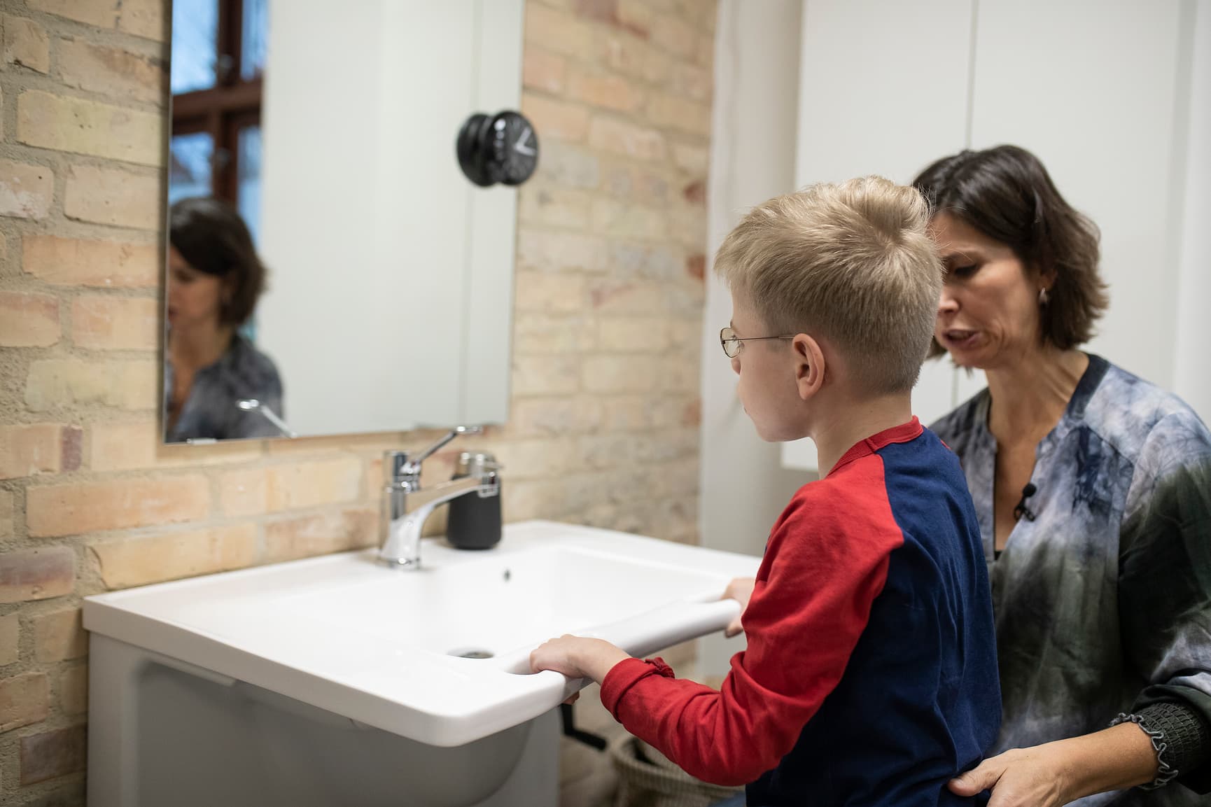 Height adjustable wash basin in use by a boy and his mother